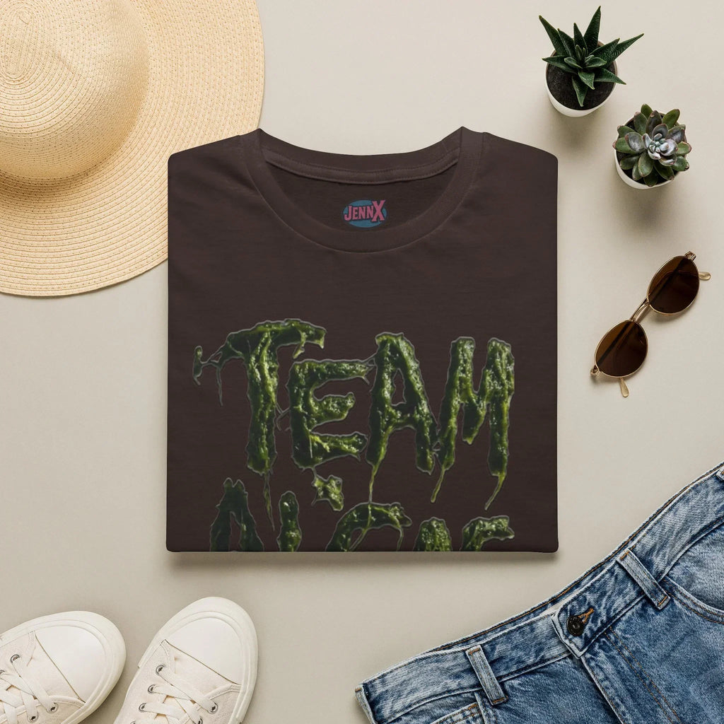 Dark brown protest tee with dripping green 'TEAM' text, styled with hat, jeans, and succulents.