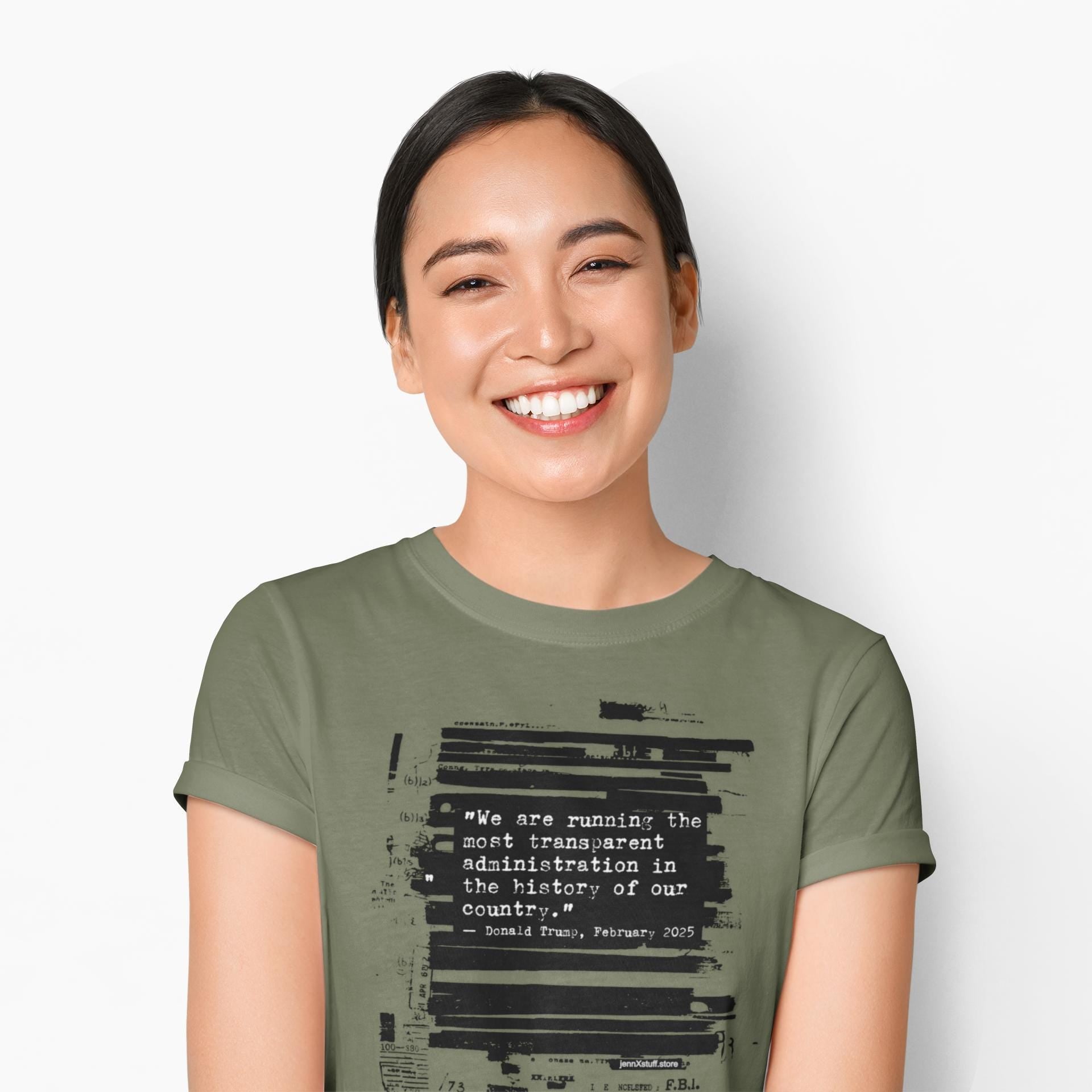 May include: Olive green t-shirt featuring a quote attributed to Donald Trump, with the text "We are running the most transparent administration in the history of our country." The quote is overlaid on a background of redacted documents.