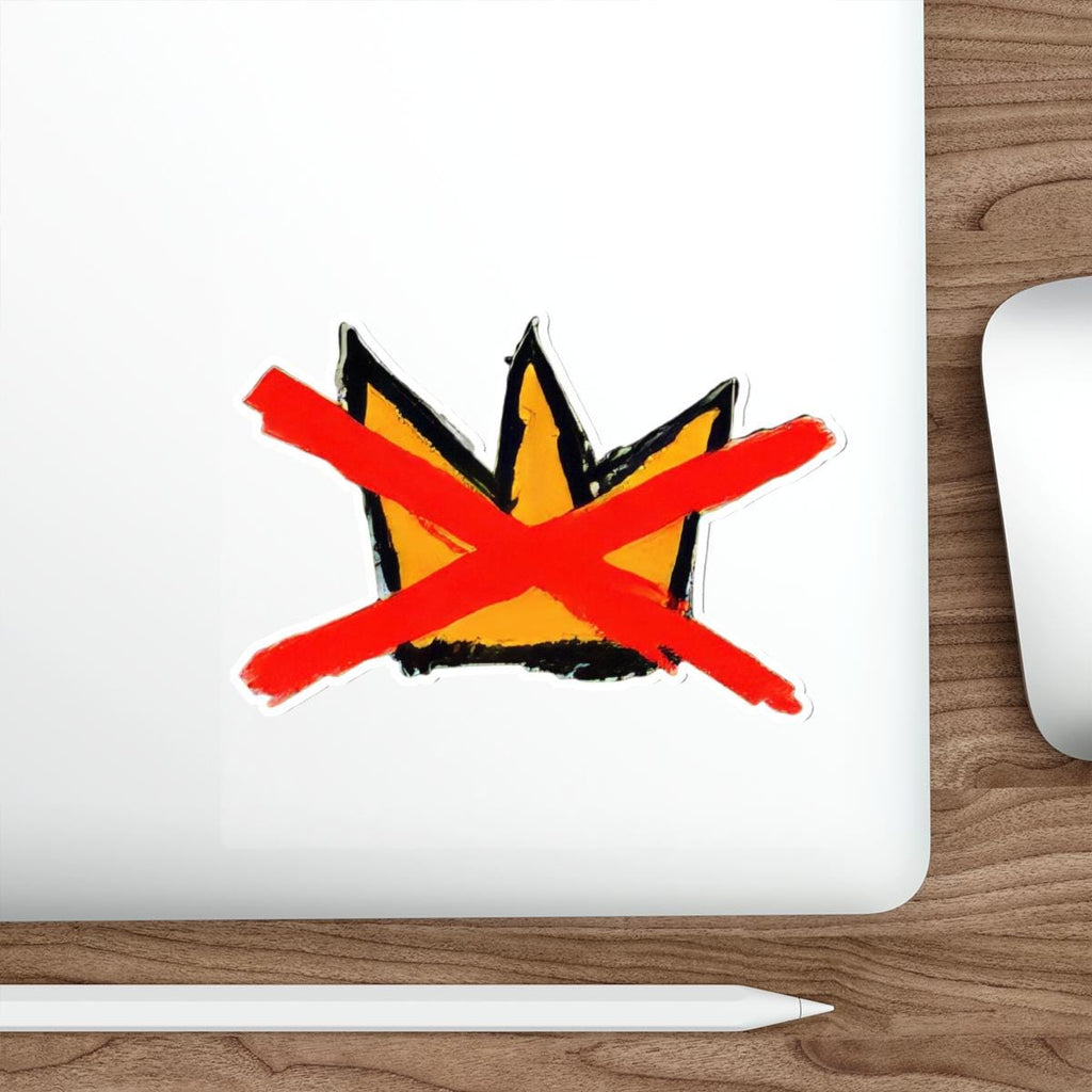May include: A sticker featuring a stylized crown design in yellow and black, crossed out with a bold red X. The sticker is on a white surface, with a wooden background visible.