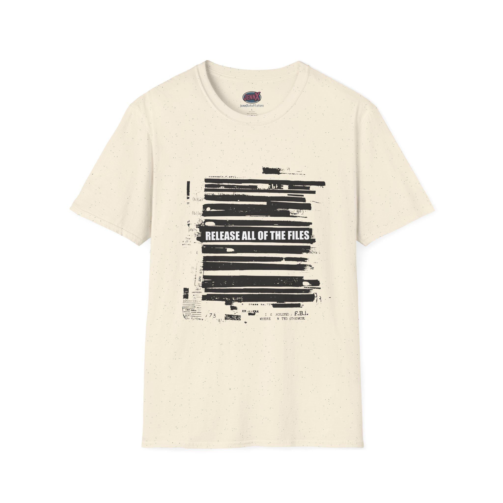 May include: Cream-colored t-shirt with a crew neck. The front features a black graphic resembling redacted documents, with the text "RELEASE ALL OF THE FILES" in white. The shirt has a speckled texture.