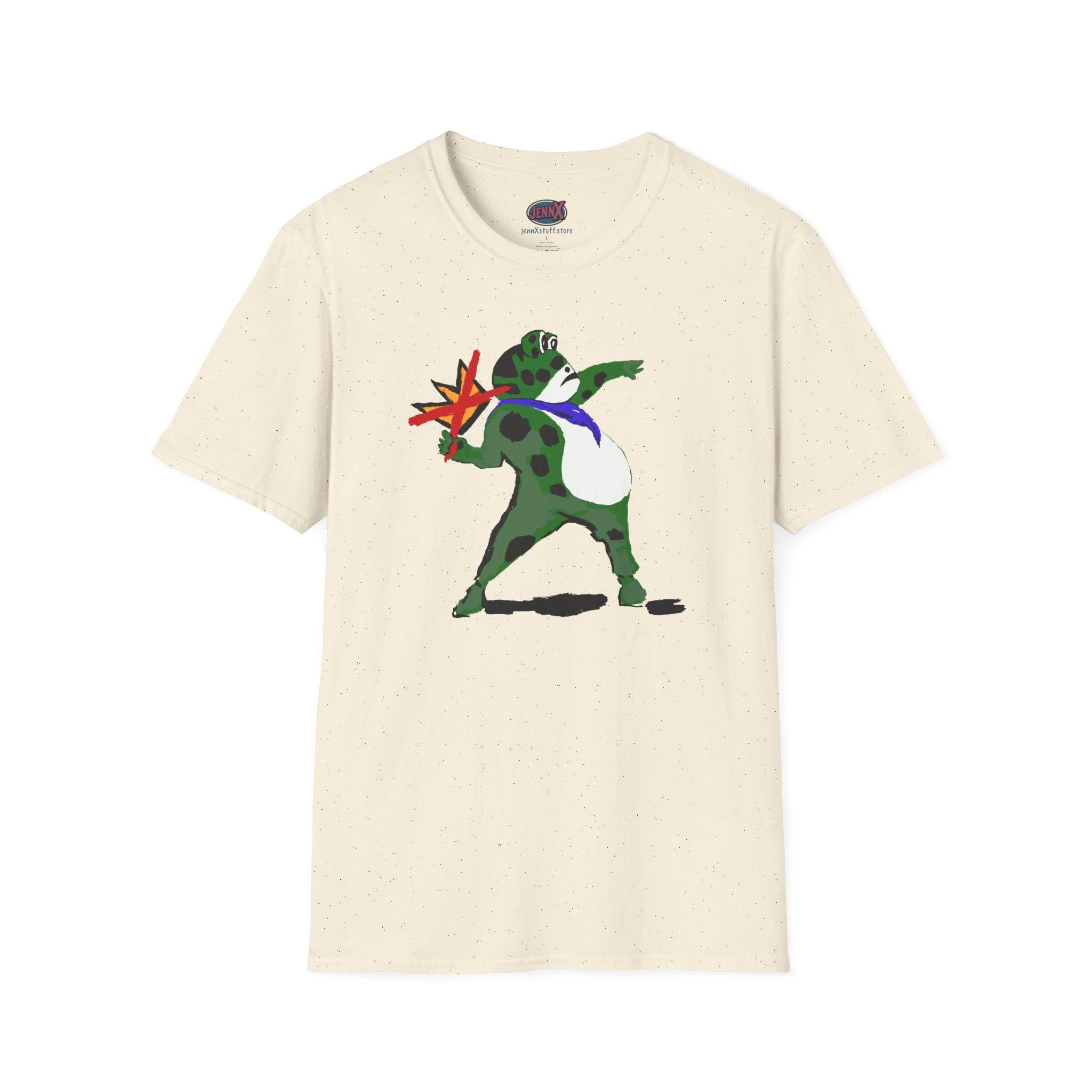 May include: Cream-colored t-shirt featuring a cartoon frog with green spots, a blue tie, and a white belly. The frog is throwing a red and yellow star-shaped object. The shirt has a crew neck and short sleeves.