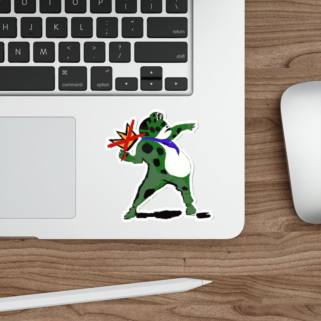 May include: A sticker featuring a green frog with black spots, wearing a blue tie, throwing a red and yellow starburst. The sticker is placed on a white laptop.