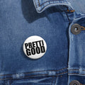 May include: A white button with the words "PRETTI GOOD" in bold, black capital letters. The button is pinned to a blue denim jacket. The button is round and has a glossy finish.