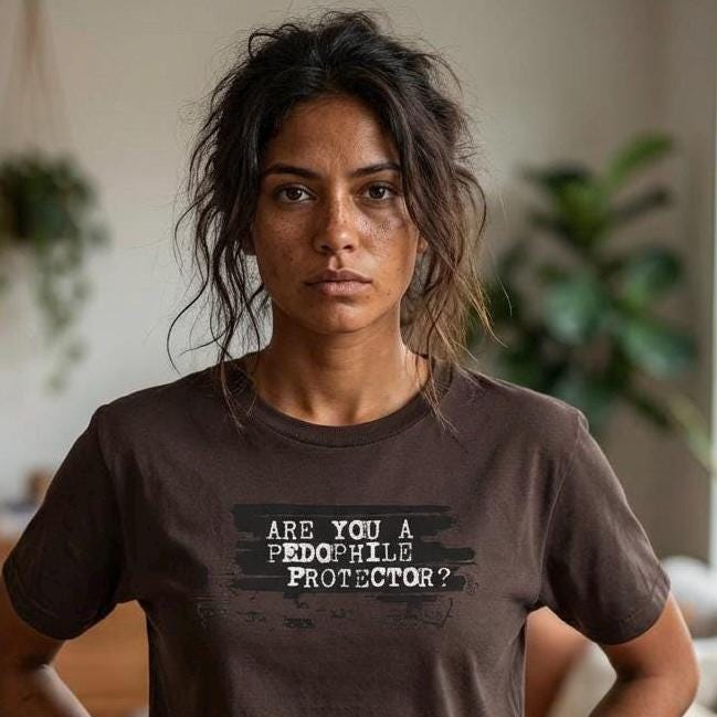 May include: A brown t-shirt with the text "ARE YOU A PEDOPHILE PROTECTOR?" in a distressed, white font. The shirt is worn by a person with dark hair and is paired with dark jeans.