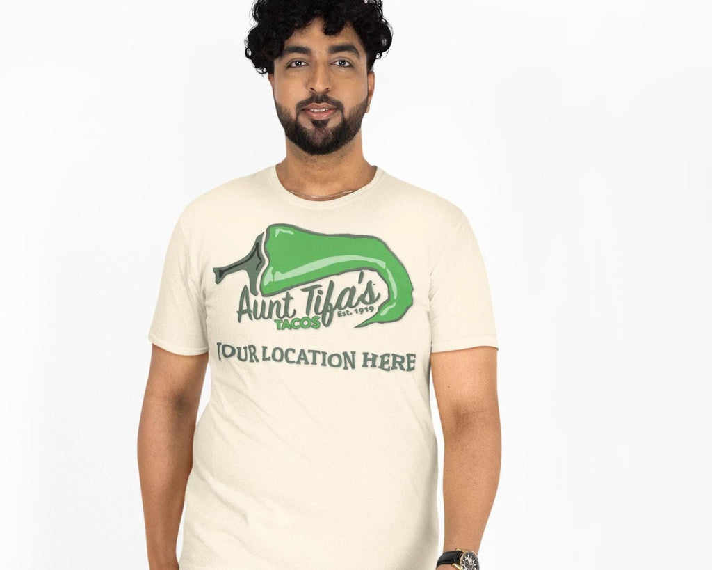 Aunt Tifa’s Tacos parody restaurant T-shirt with a customizable city name on white cotton fabric. Flat-front layout featuring the bold green-chili logo design. Satirical streetwear graphic for adults who love ironic humor and customizable parody merch.